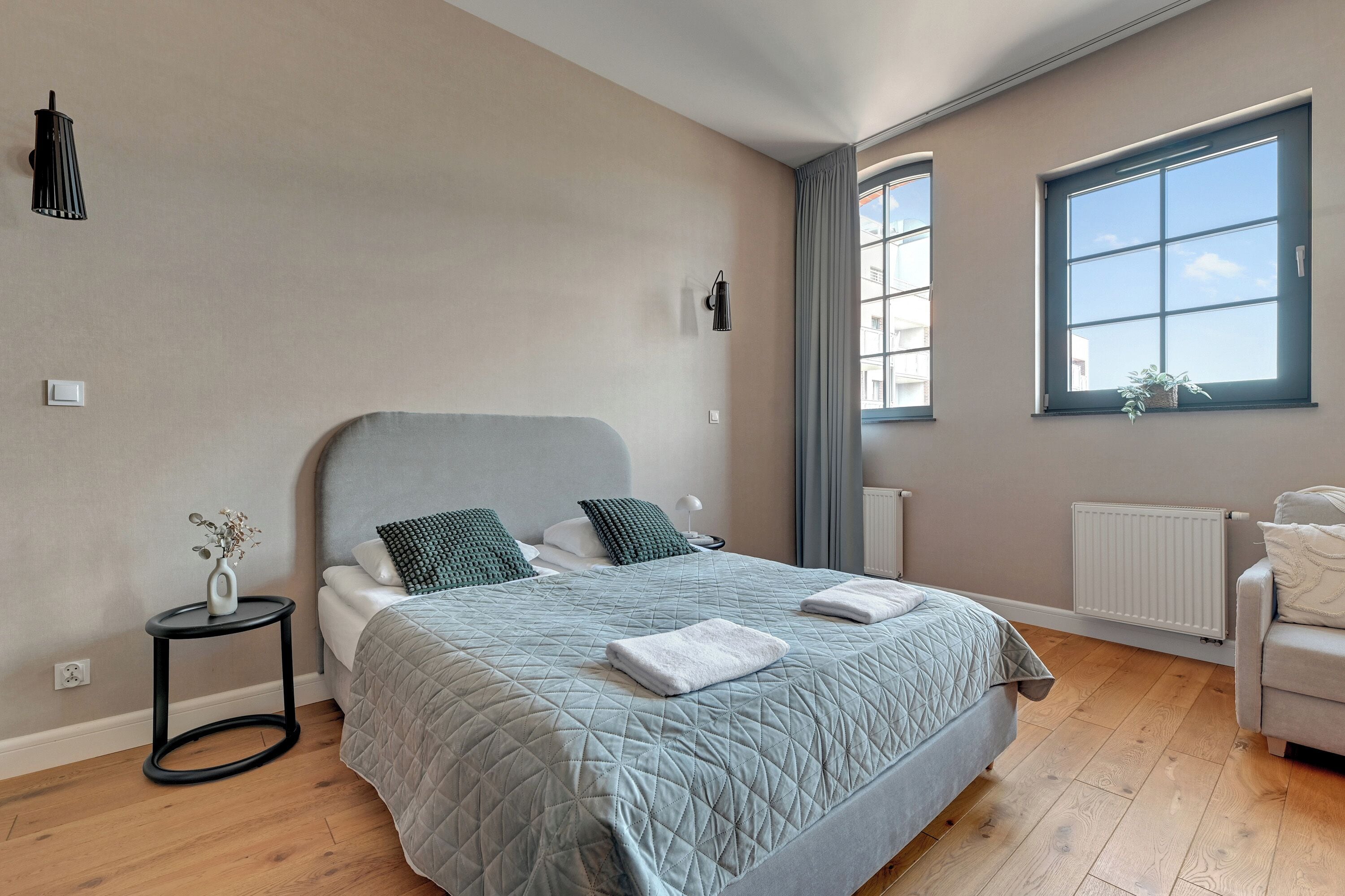 A bedroom with a bed, a side table, a chair, a window, and a radiator.