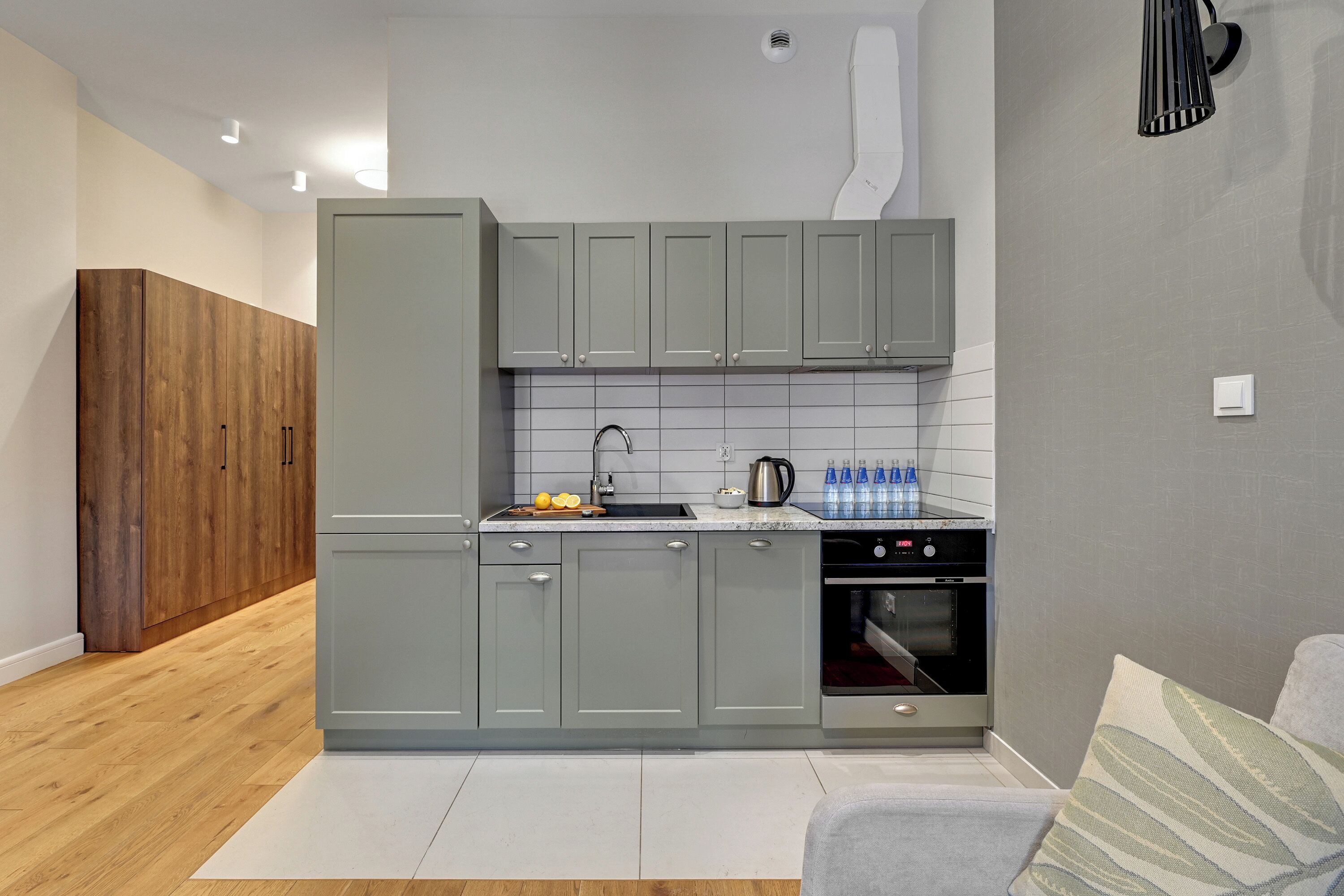 A modern kitchen with grey cabinets, a wooden floor, and a built-in oven.