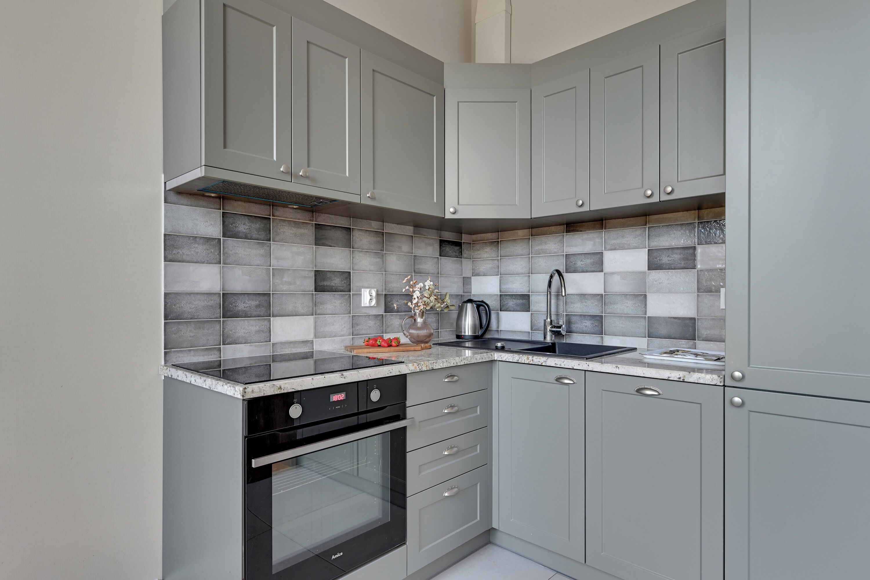 Cocina compacta con gabinetes grises, horno negro y salpicadero de azulejos.