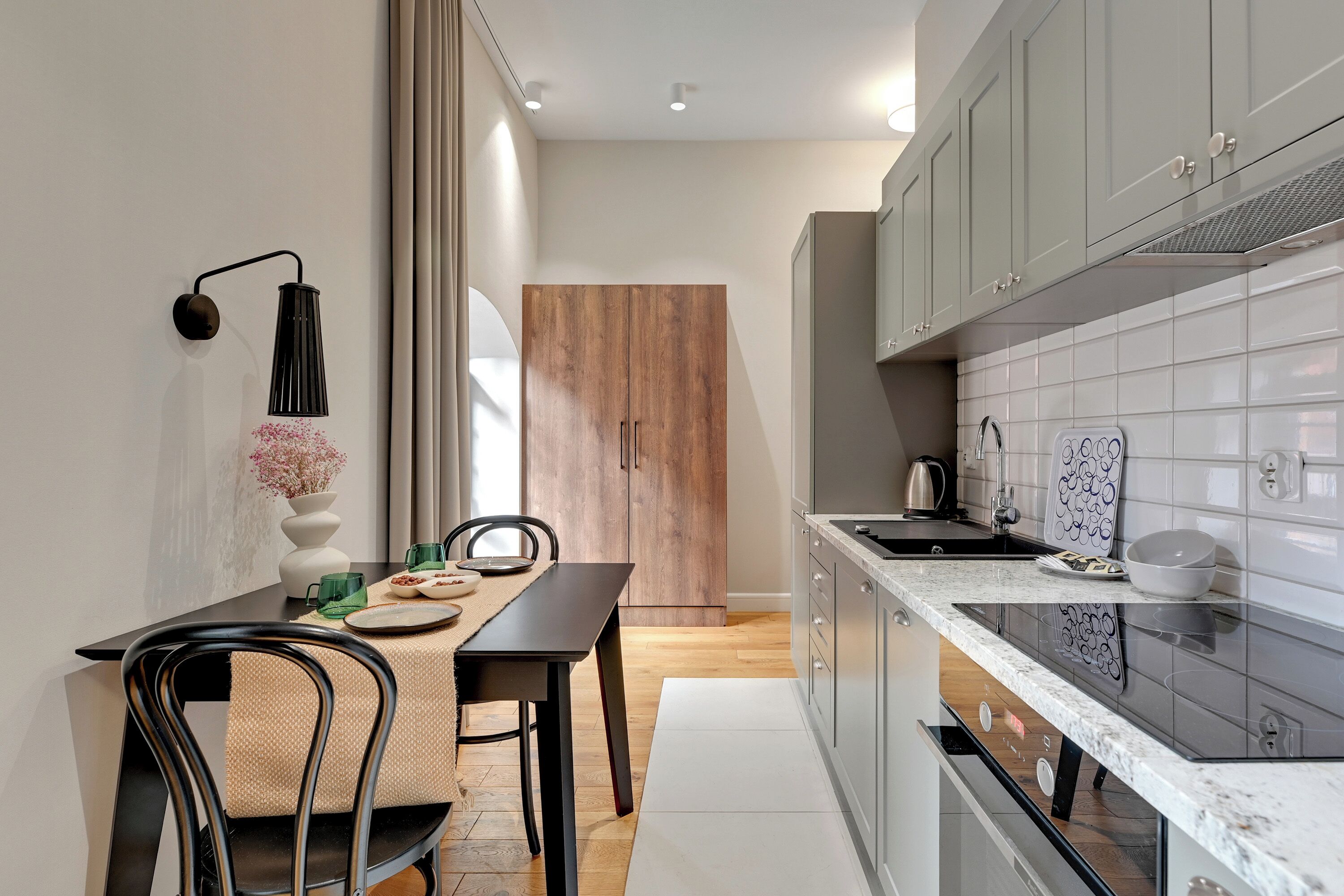 A modern kitchen with a dining area, featuring a wooden door, white tiled backsplash, and a black countertop.