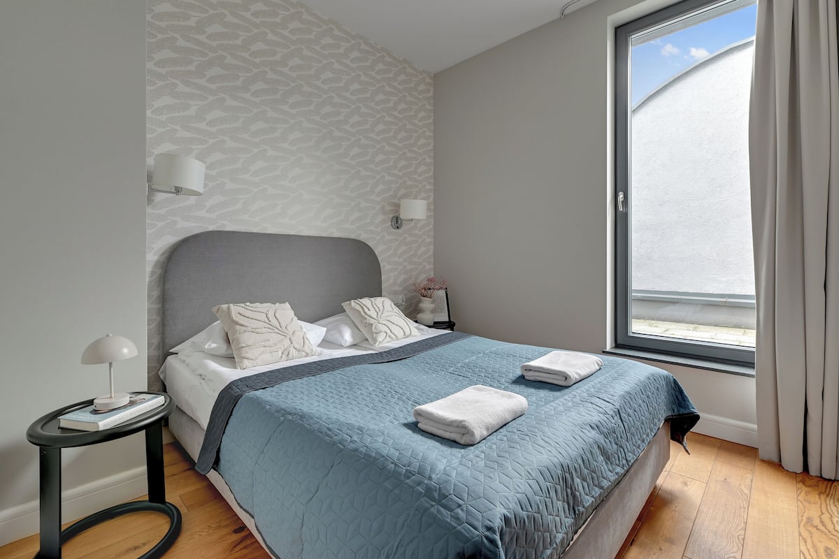 Ein modernes Schlafzimmer mit einem großen Bett, einem Nachttisch, einem Fenster mit Vorhängen und einer Wand mit Muster.