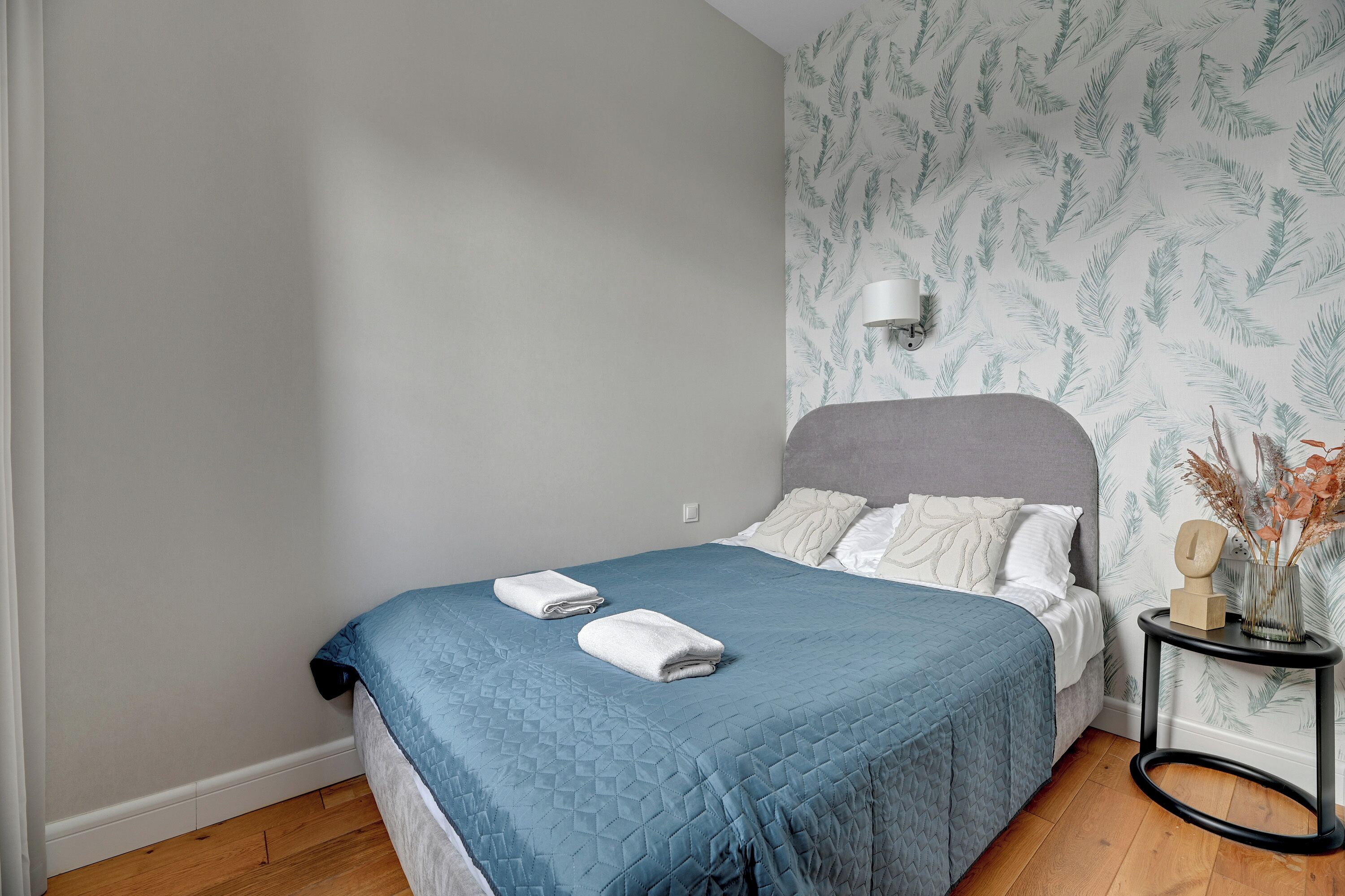A neatly made bed with a blue quilt, white pillows, and two folded towels on the side.