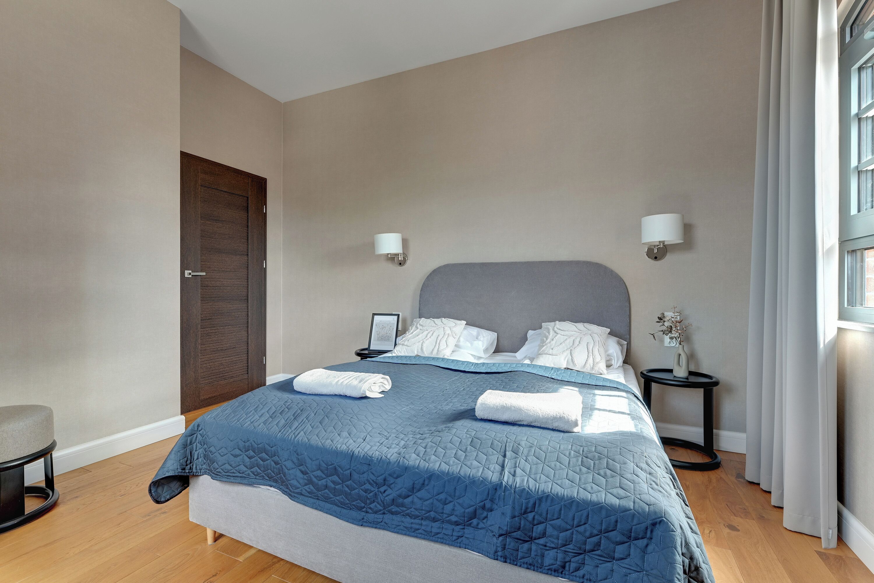 Een moderne slaapkamer met een groot bed, twee nachtkastjes, een stoel en een deur.