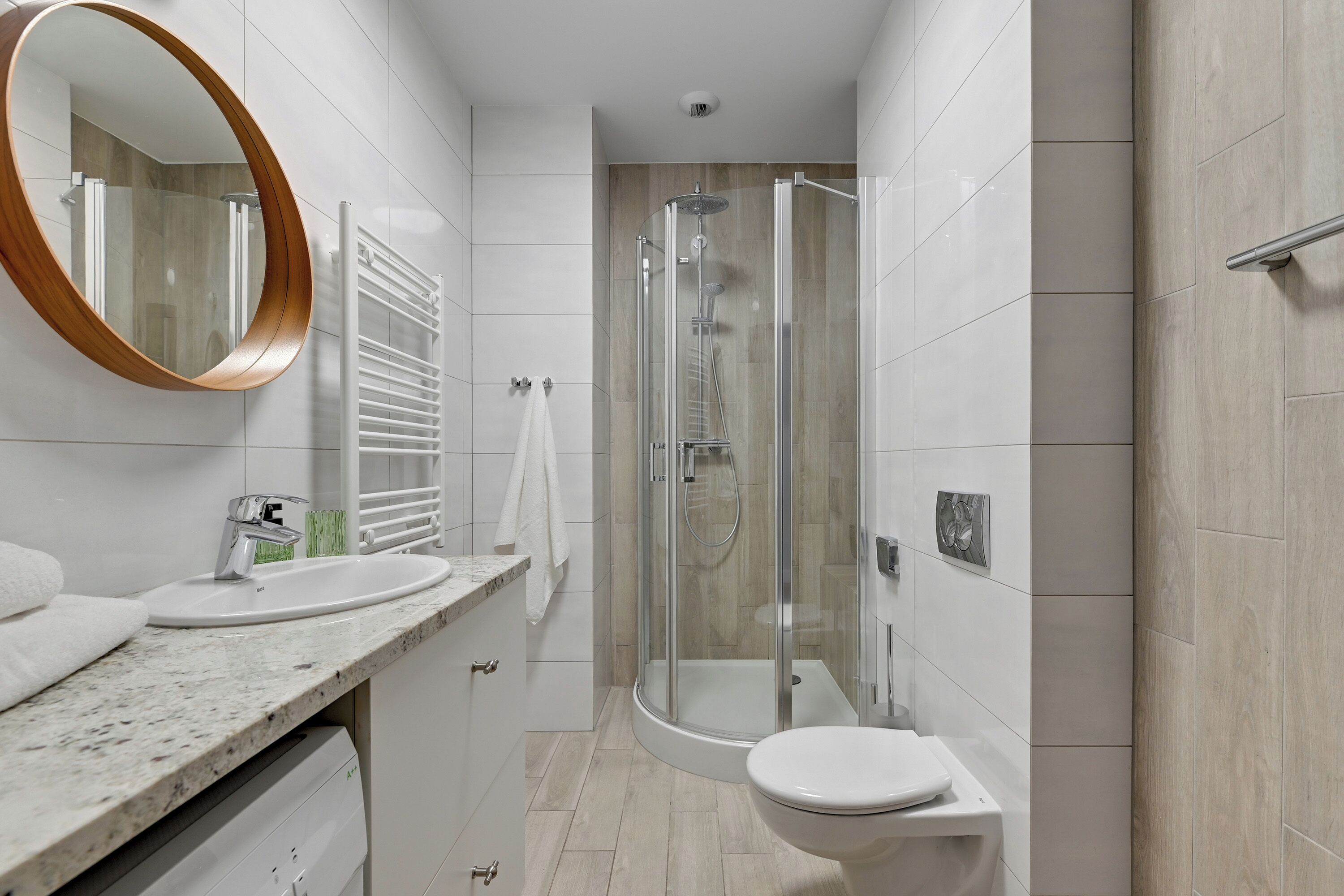 Un baño moderno con ducha de vidrio, lavabo blanco y un espejo grande.