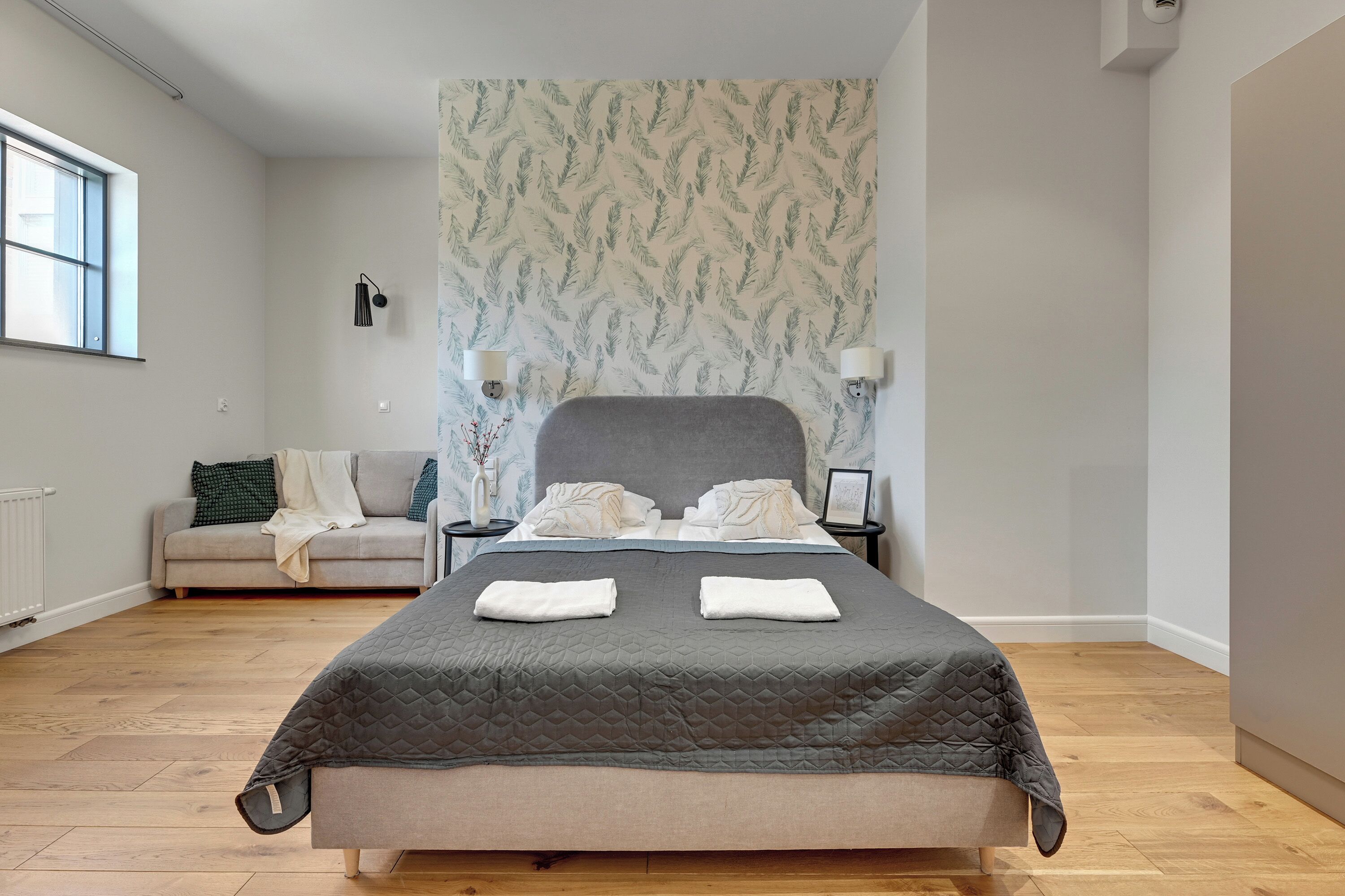 A modern bedroom with a large bed, a sofa, and a patterned wallpaper.