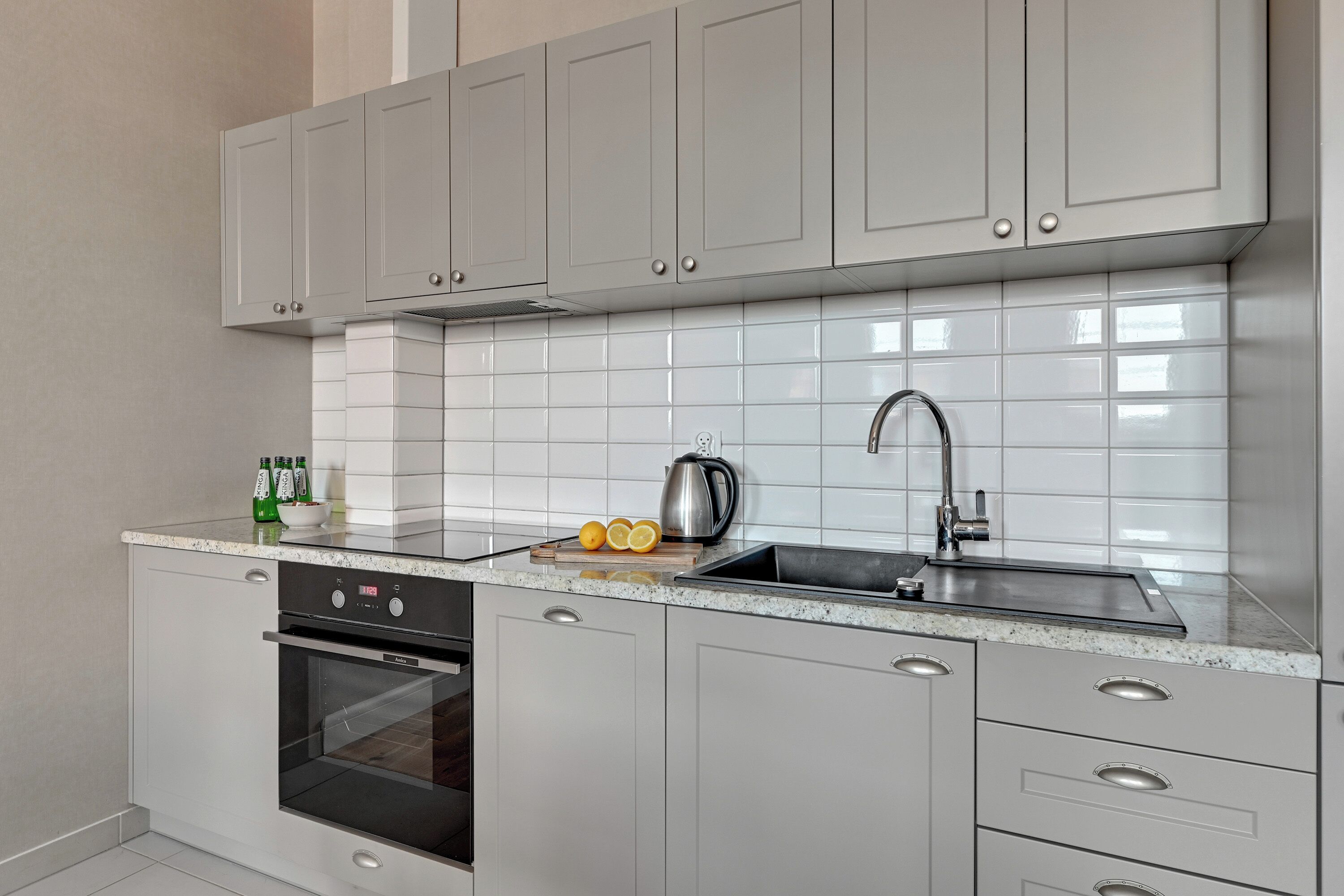 A modern kitchen with grey cabinets, a stainless steel sink, and a built-in oven.