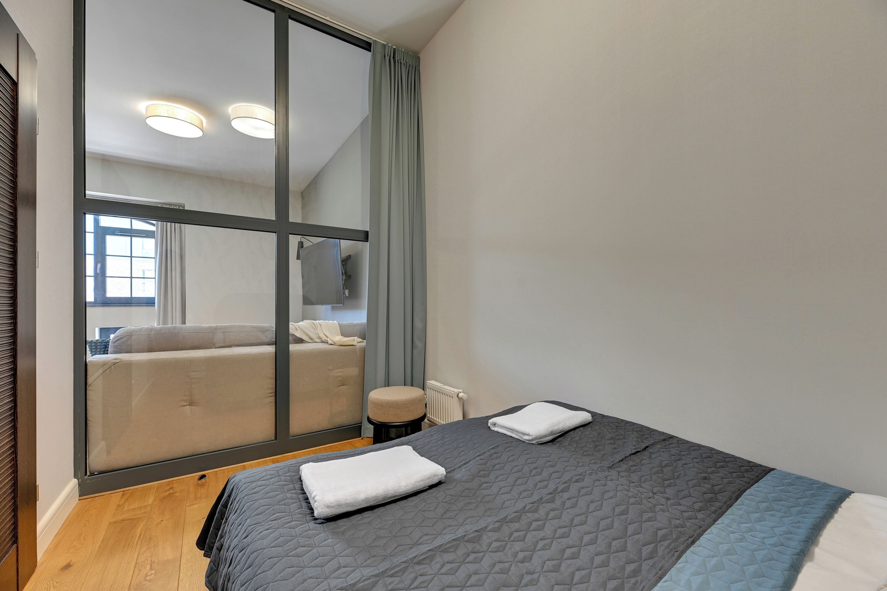 Quarto moderno com uma grande porta de vidro deslizante que dá para uma varanda, uma cama com cobertura acolchoada e um pequeno banquinho.