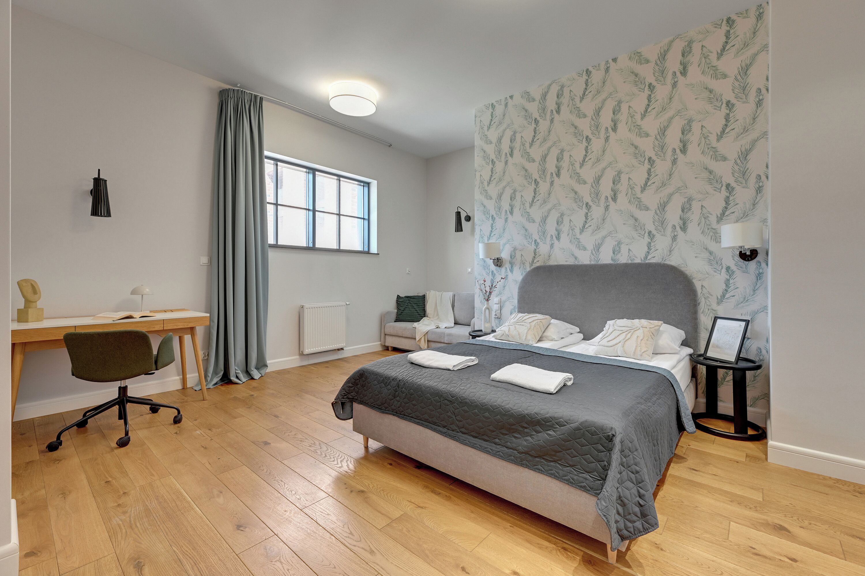 Un dormitorio con una cama, un escritorio, una silla, un ventanal y una pared con diseño.