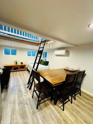 Un comedor con mesa y sillas de madera, una zona de descanso en un altillo, y una pequeña cocina americana.