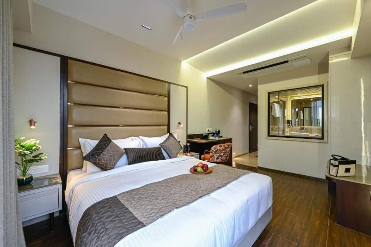 A modern hotel room with a large bed, a desk, a chair, and a mirror.