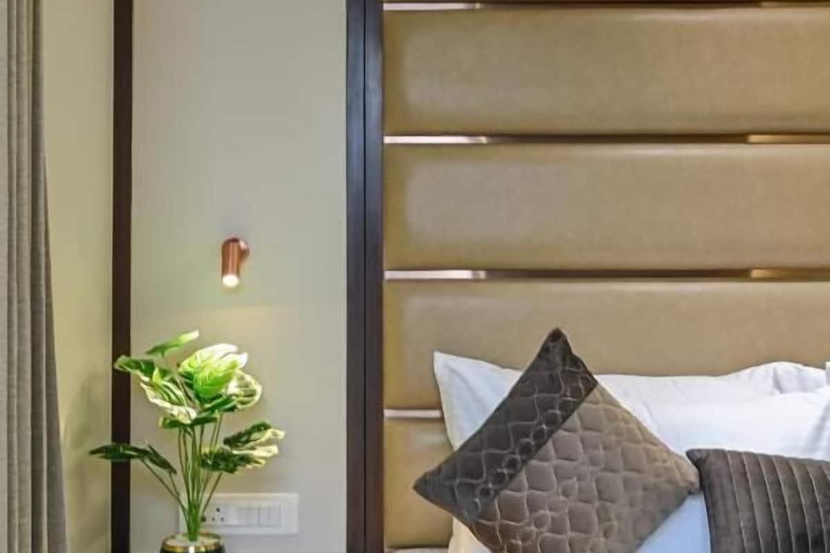 A neatly made bed with a headboard, a bedside table with a lamp and a plant, and a wall-mounted light fixture.
