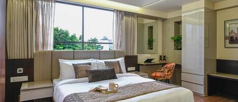Une chambre d’hôtel moderne, dotée d’un grand lit, d’un bureau, d’une chaise et offrant une vue sur la verdure environnante.