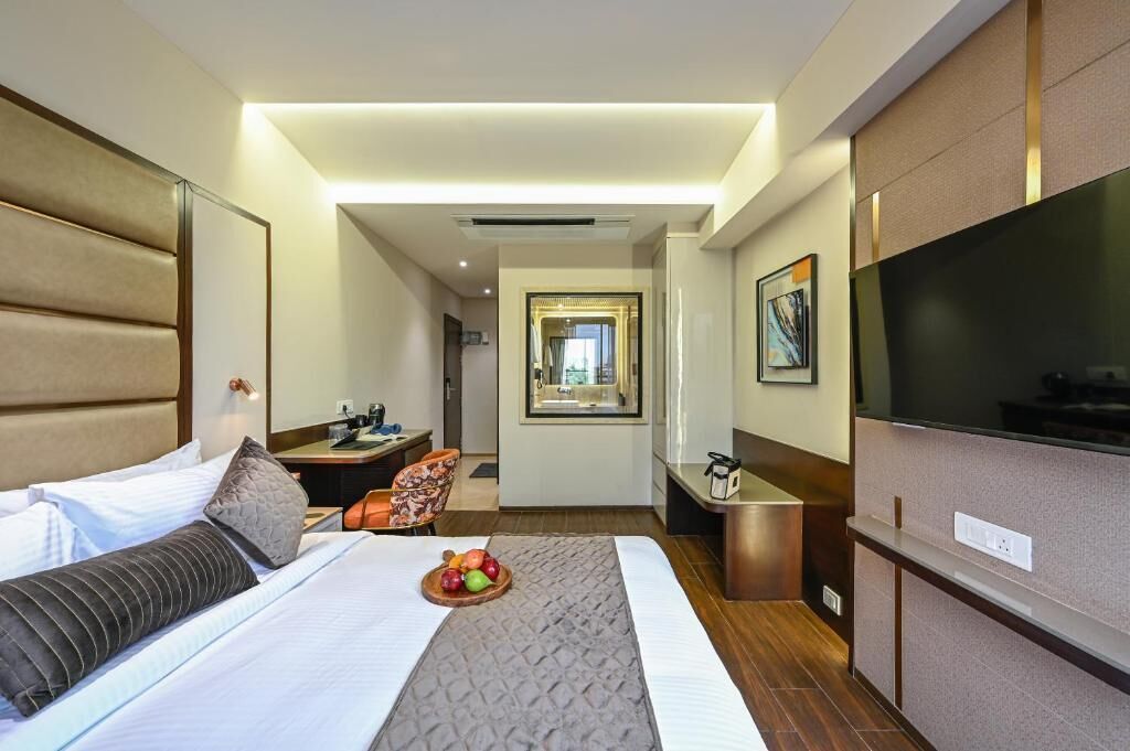 A hotel room with a bed, a desk, a chair, a TV, and a fruit basket on the bed.