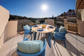 Mesa redonda posta para dois, com cadeiras de vime azuis e vista para os edifícios e colinas ao redor.