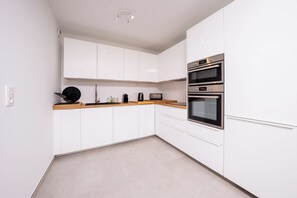 A modern kitchen with white cabinets, a wooden countertop, and two built-in ovens. - Féeries Provençales 223 by Avecoeur (Grimaud)