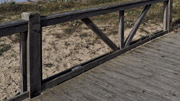 A wooden boardwalk leading to a beach with waves in the background.