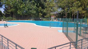 A swimming pool with a tiled deck, surrounded by a green fence, and trees in the background.
