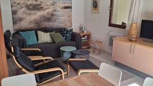 A cozy living room with a sofa, chairs, a dining table, and a painting of a beach scene.