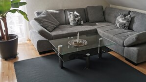 A modern living room with a grey sectional sofa, a glass coffee table, and a potted plant. - Deluxe vacation apartment / near Willingen (Korbach)
