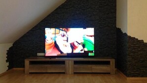 A television on a wooden stand in a room with a sloped ceiling and stone wall. - Deluxe vacation apartment / near Willingen (Korbach)