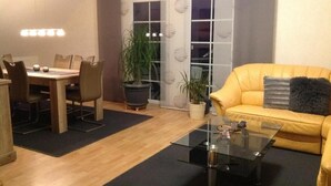 A living room with a yellow sofa, a glass coffee table, and a dining area with a wooden table and chairs. - Deluxe vacation apartment / near Willingen (Korbach)
