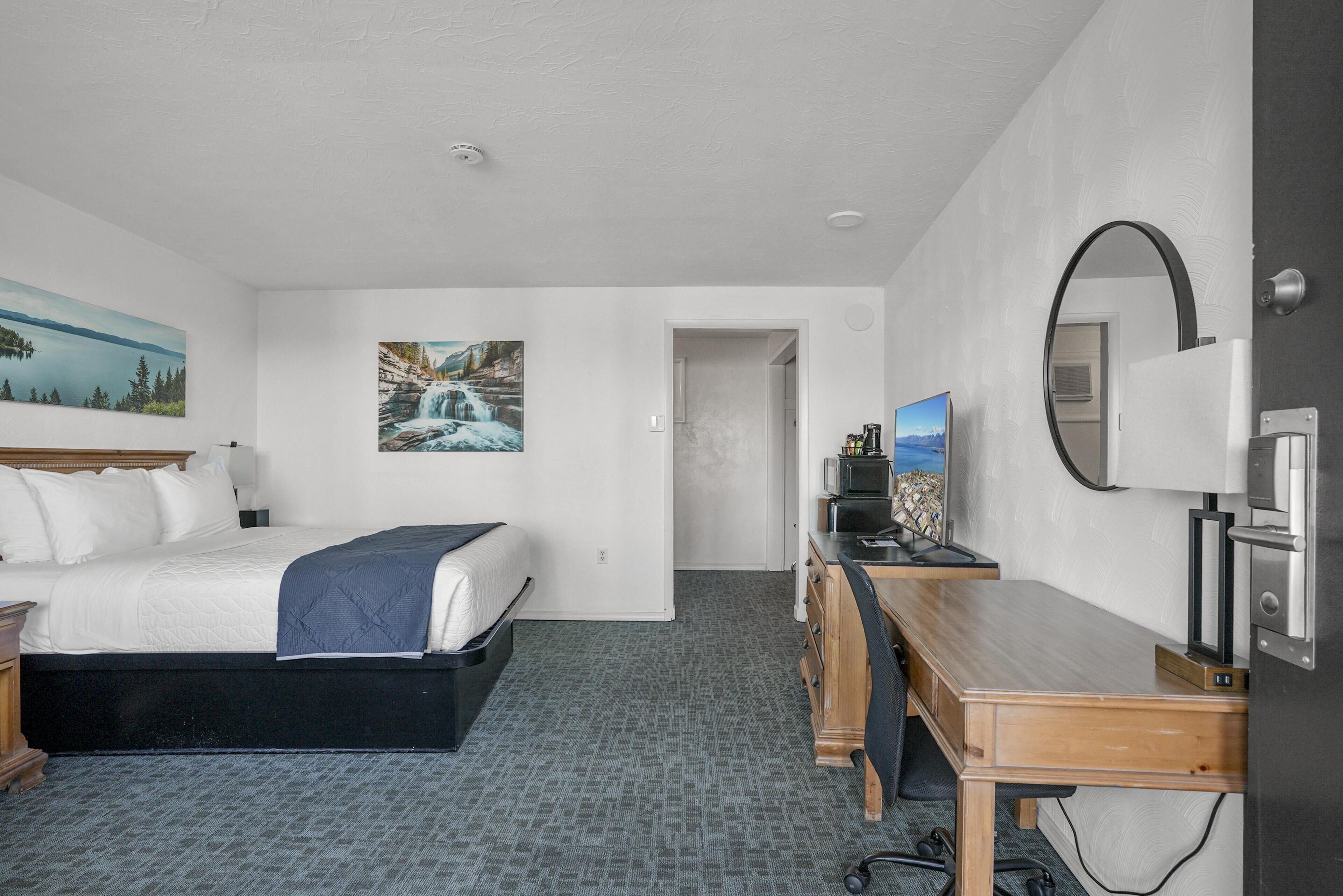 A hotel room with a bed, desk, and two paintings on the walls.