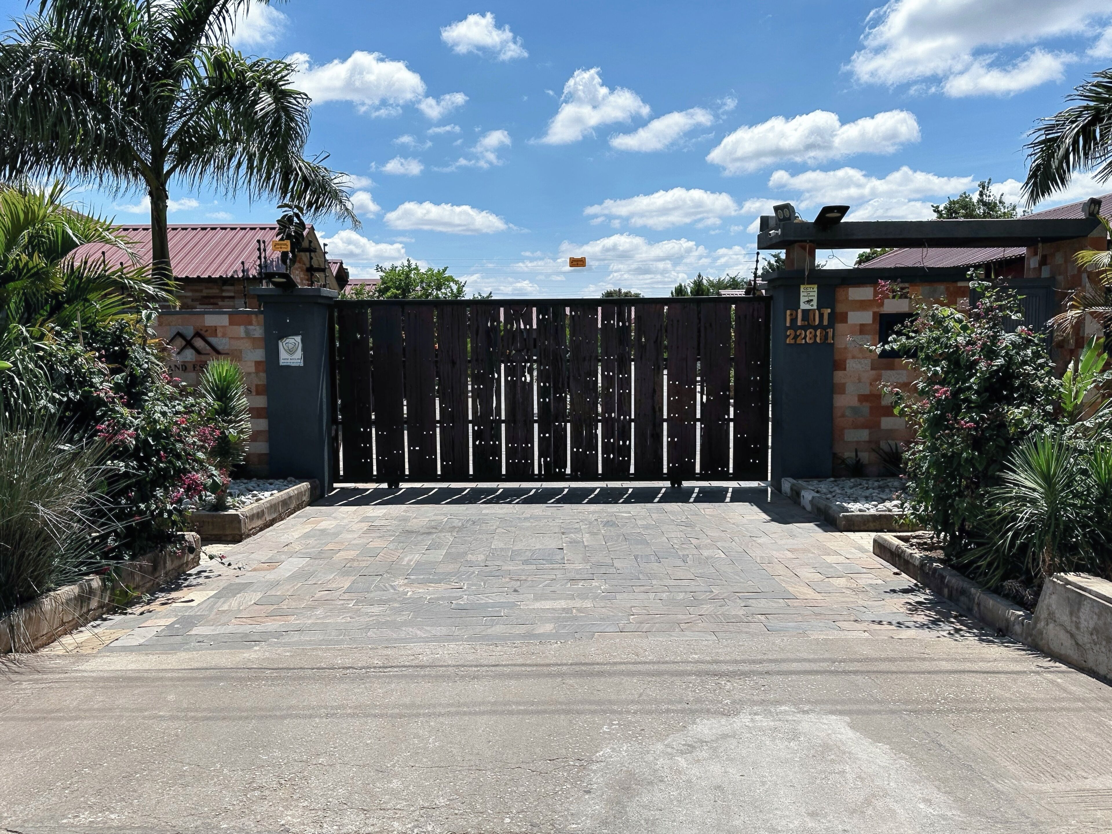 A gated entrance with a metal gate, a brick wall, and a sign indicating a plot number.
