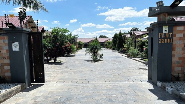 A paved pathway leading to a gated entrance with a sign indicating 'Plot 22801'. - Upland Serviced Apartments (Lusaka)