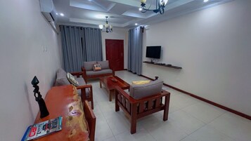 Una sala de estar con sofá, sillón, mesa de centro y televisor montado en la pared.