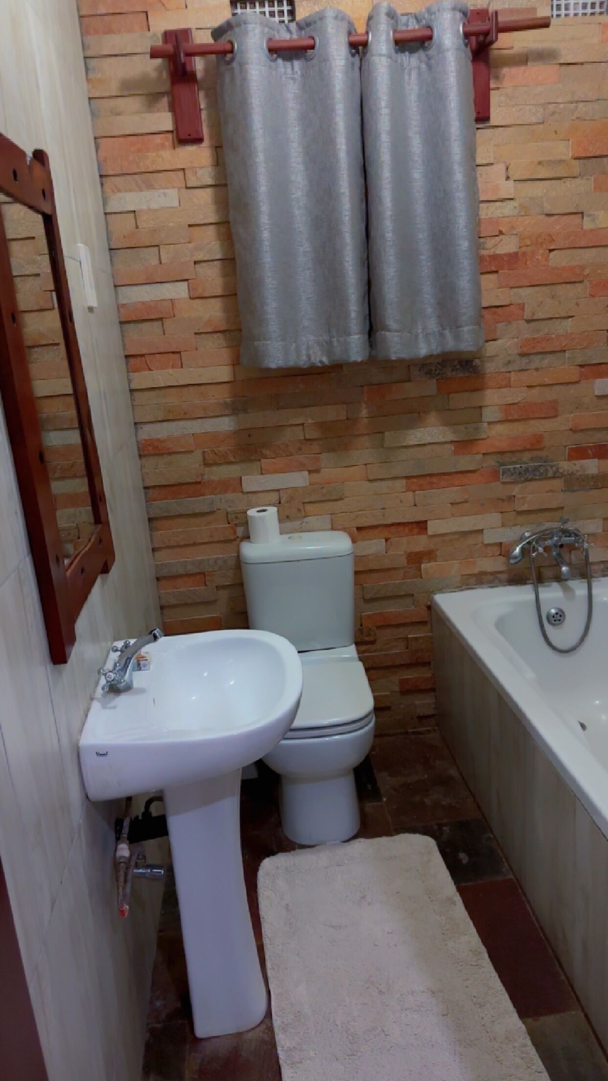 A bathroom with a white sink, toilet, and bathtub. There is a mirror on the wall and a towel on the floor.