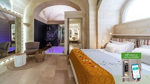 A luxurious hotel room with a large bed, a sitting area with a chair and a small table, a mirror, and a bathroom visible through an archway. - Corte Dei Granai Meeting&SPA Raro Rooms (Maglie)