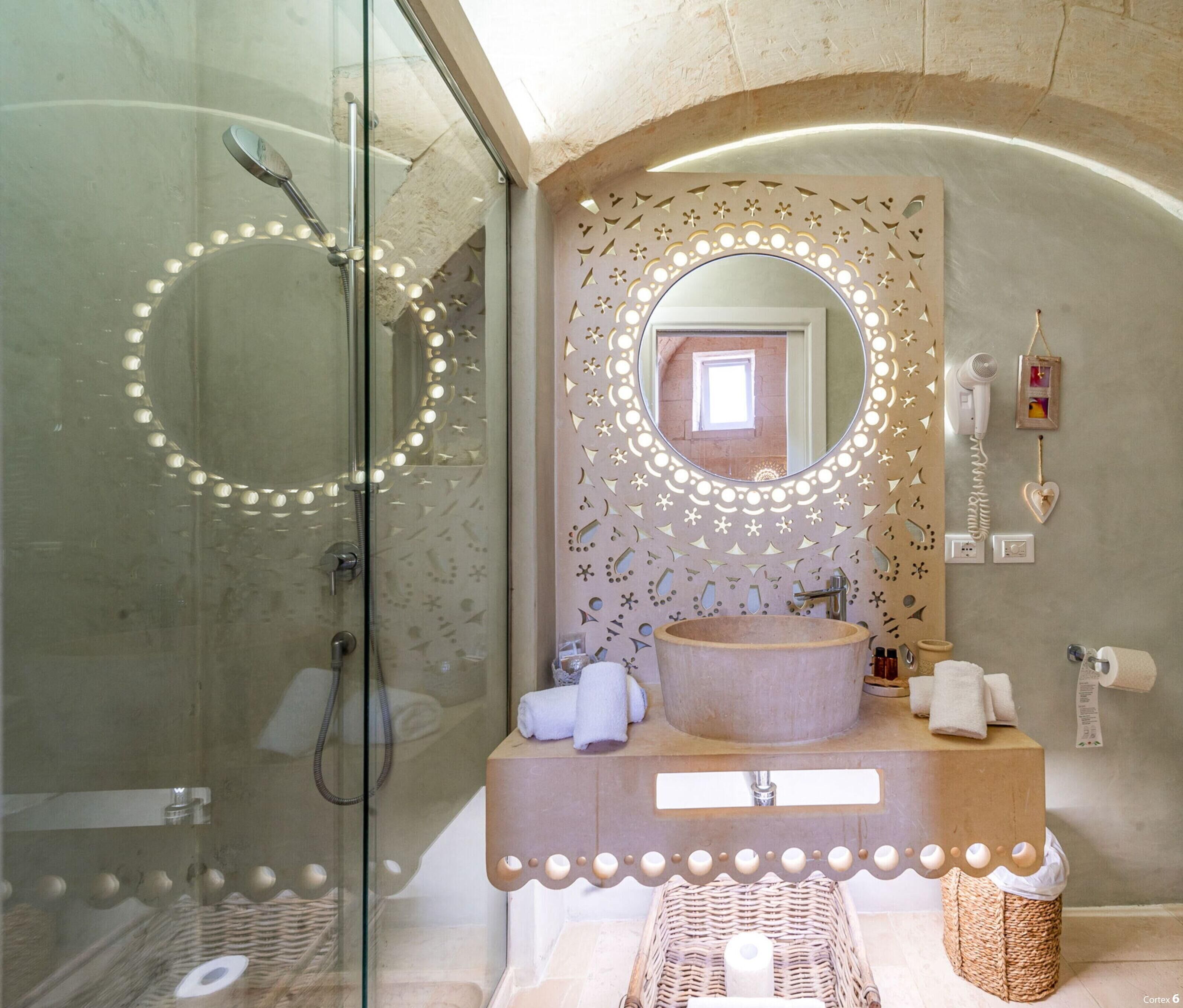 Un baño con cabina de ducha de vidrio, tocador con espejo redondo y secador de pelo de pared.