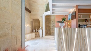 A modern lobby with stone walls, a reception desk, and a kitchen area visible in the background. - Corte Dei Granai Meeting&SPA Raro Rooms (Maglie)