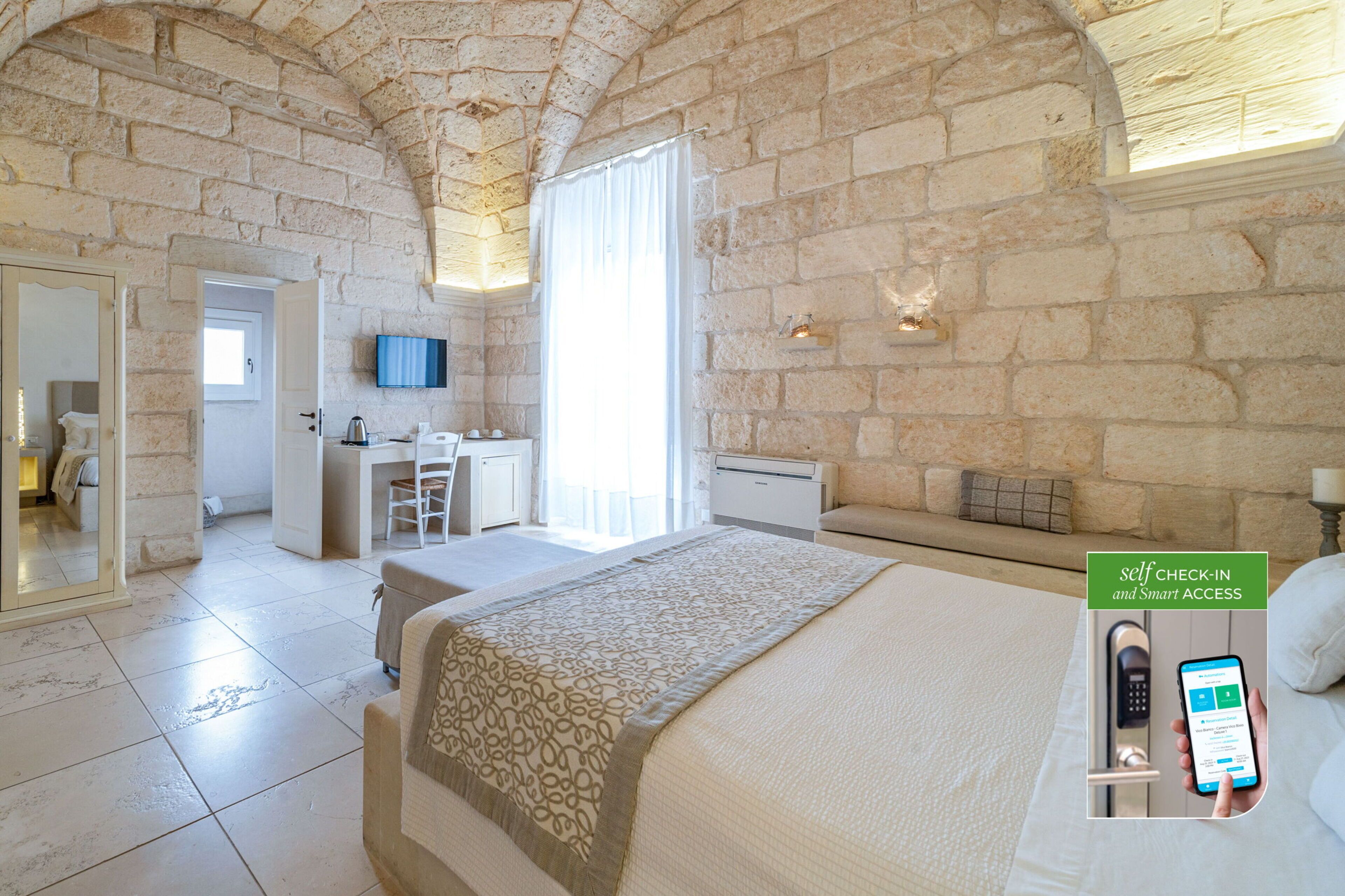 A hotel room with a stone wall, a bed, a desk, and a bathroom.