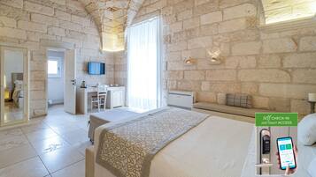 Quarto de hotel com parede de pedra, uma cama, uma escrivaninha e um banheiro.