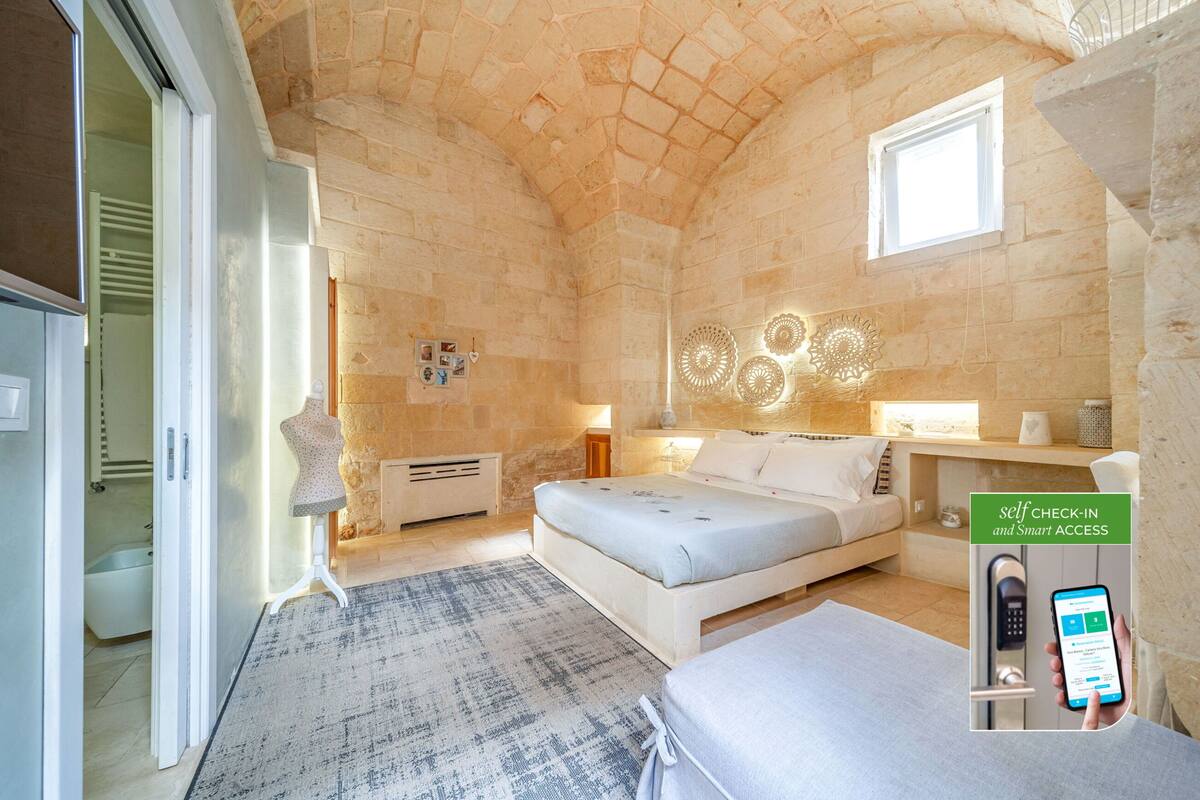 A modern bedroom with a stone wall, a bed, a bedside table, and a self-check-in system.