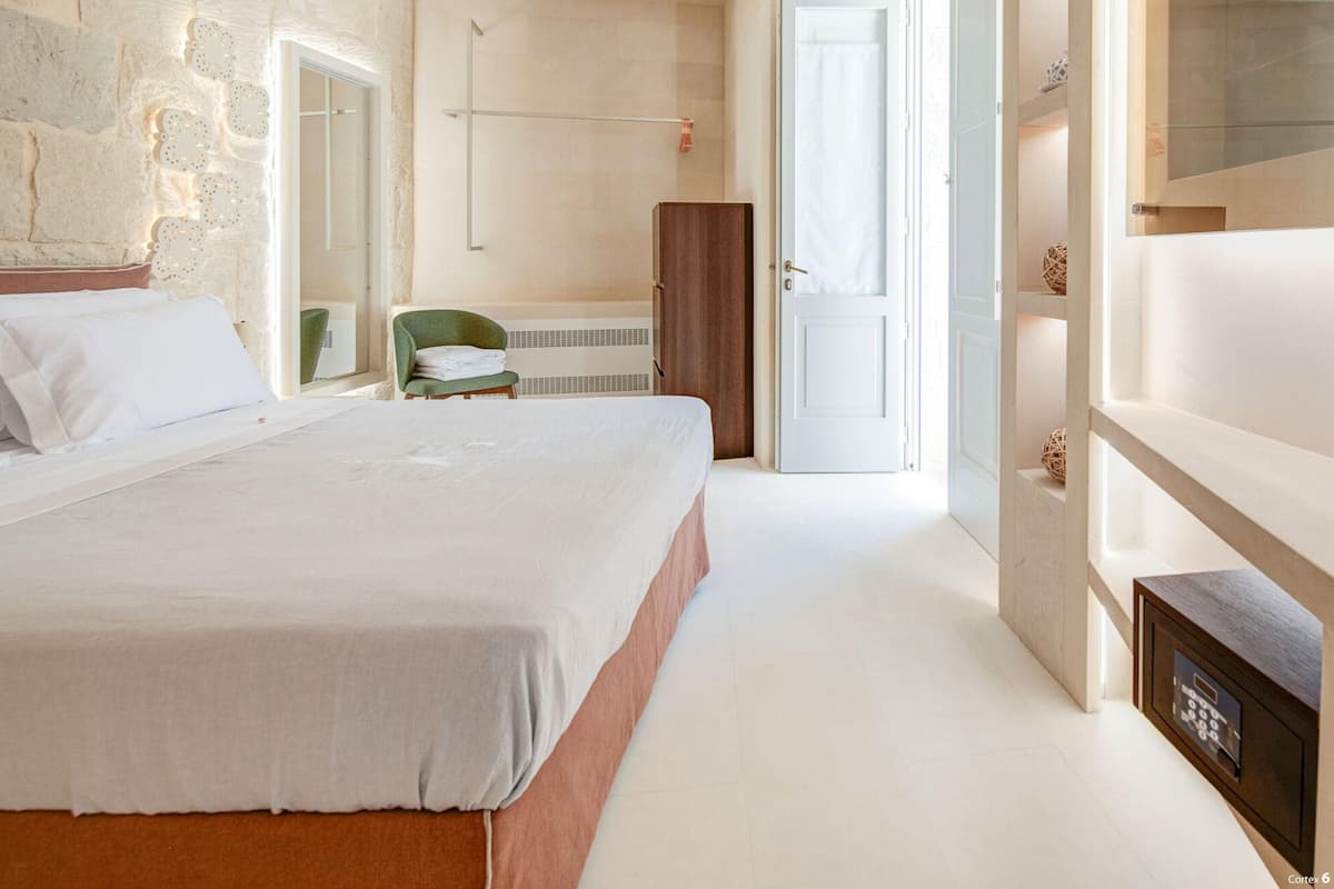 A bedroom with a large bed, a wardrobe, a chair, and a door leading to another room.