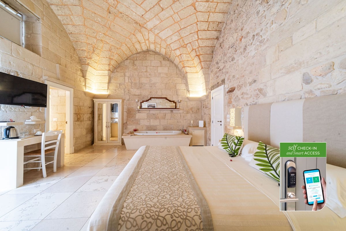 A modern hotel room with a stone arch ceiling, a large bathtub, a desk with a chair, and a self-check-in kiosk.