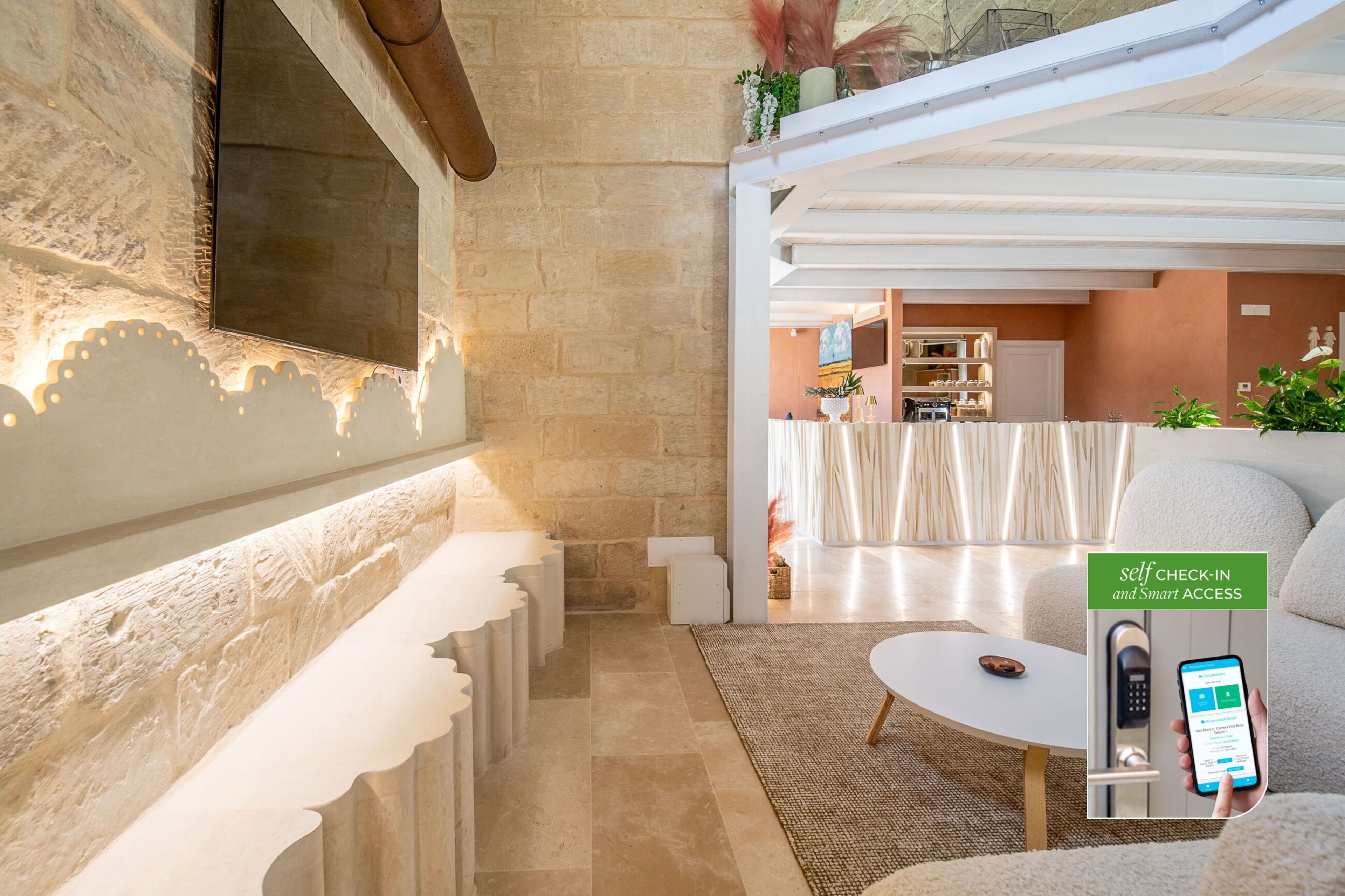 A modern hotel lobby with a self-check-in kiosk, a seating area with a white sofa, and a view of the kitchen in the background.