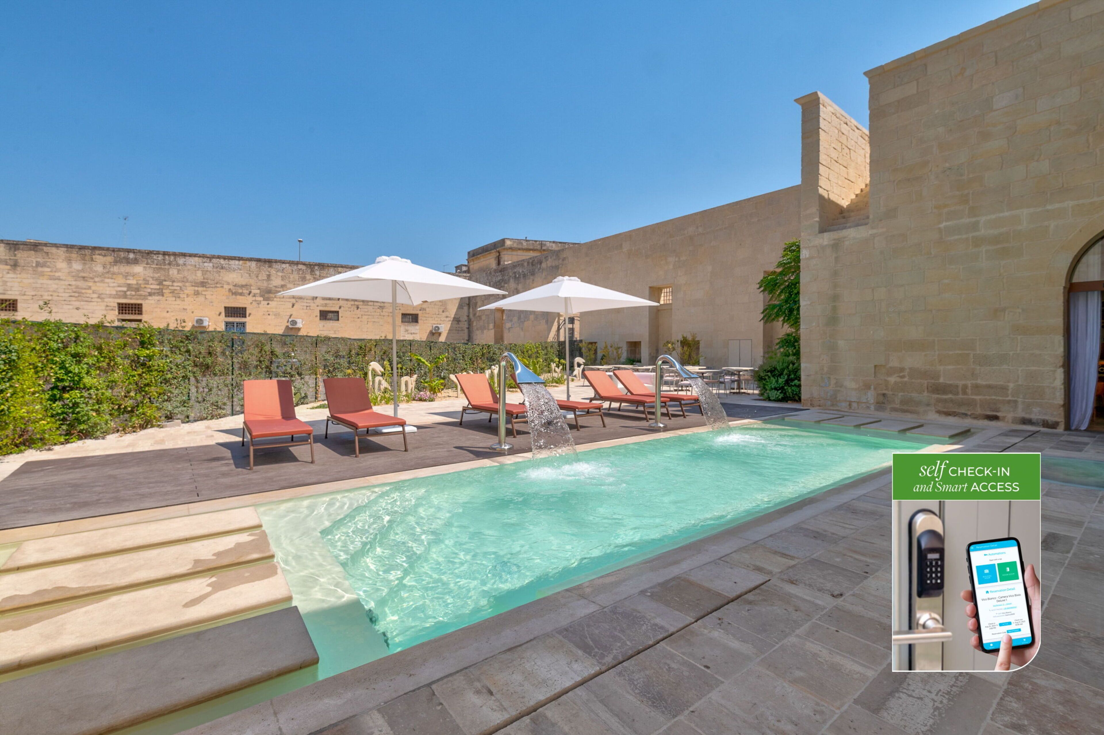 A pool area with lounge chairs and umbrellas, a self-check-in kiosk, and a stone building in the background.