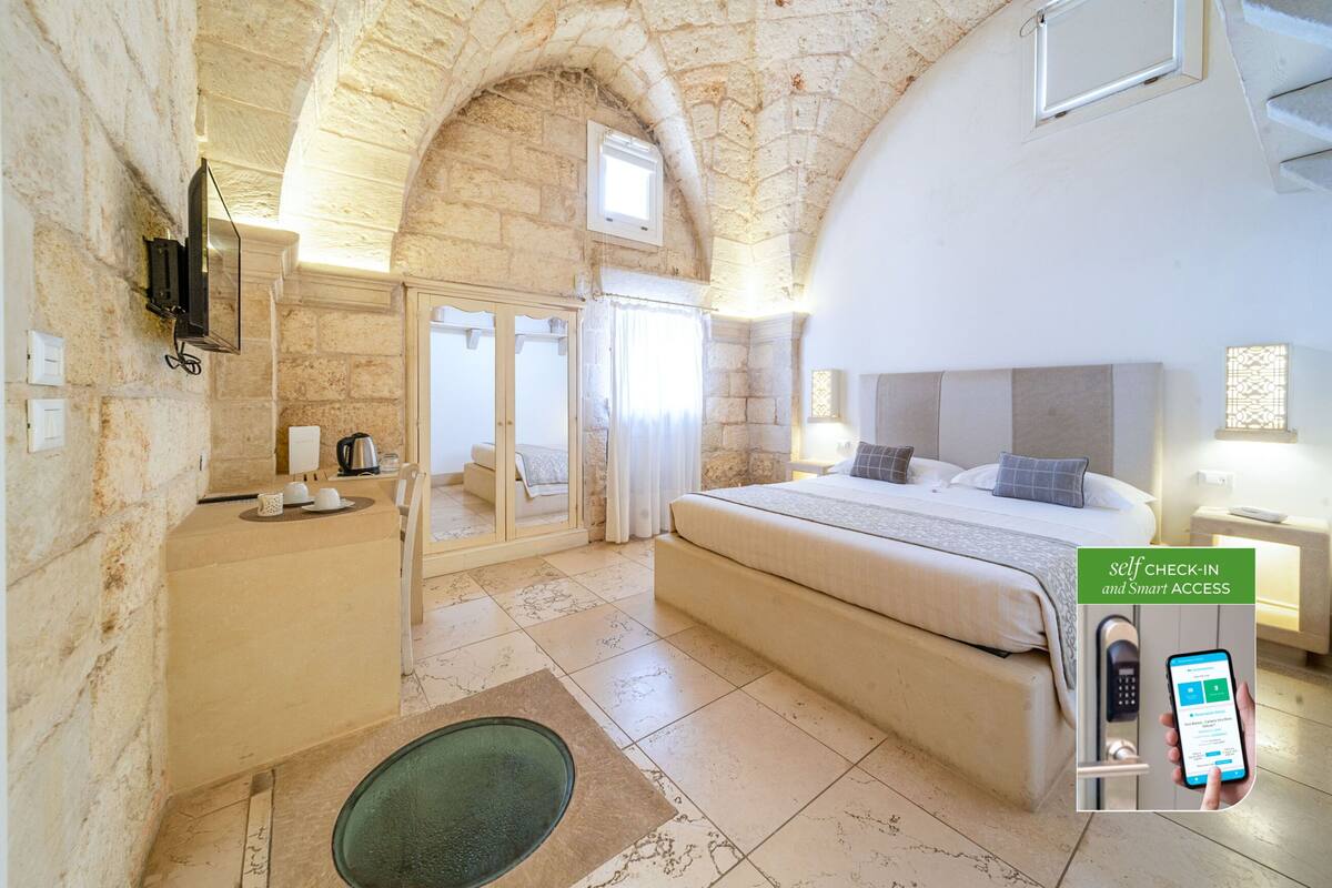 A bedroom with a stone wall, a bed, a desk, and a self-check-in system.