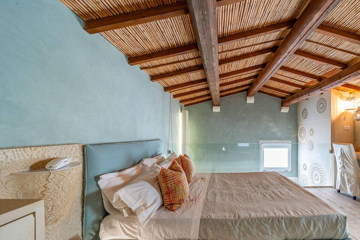 A bedroom with a large bed, a wooden ceiling, and a window.