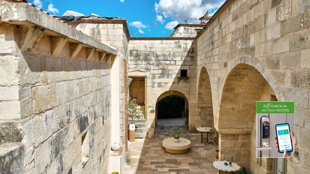 A stone courtyard with arches, a self-check-in kiosk, and a small seating area with a plant. - Corte Dei Granai Meeting&SPA Raro Rooms (Maglie)