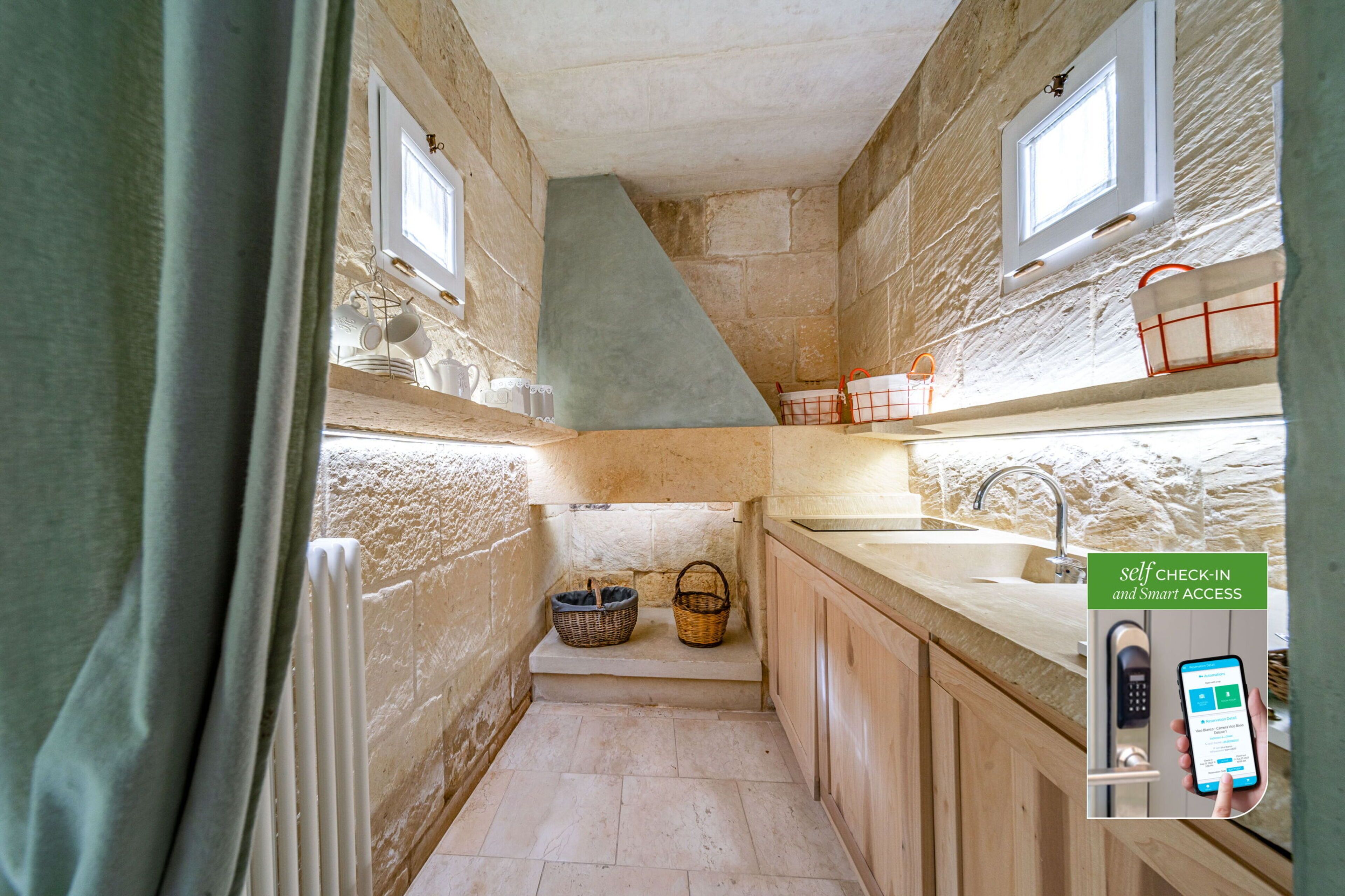 A narrow stone-walled kitchen with a built-in sink, wooden cabinets, and a window.