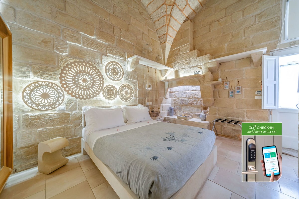 A bedroom with a stone wall, a bed with a grey floral bedspread, and a self-check-in system.