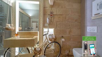 A bathroom with a stone wall, a wooden vanity, a bicycle, and a self-check-in kiosk.