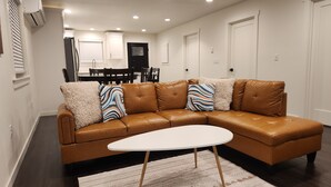 Un salon moderne avec un canapé d’angle en cuir marron, une table basse blanche et des coussins décoratifs à motifs.