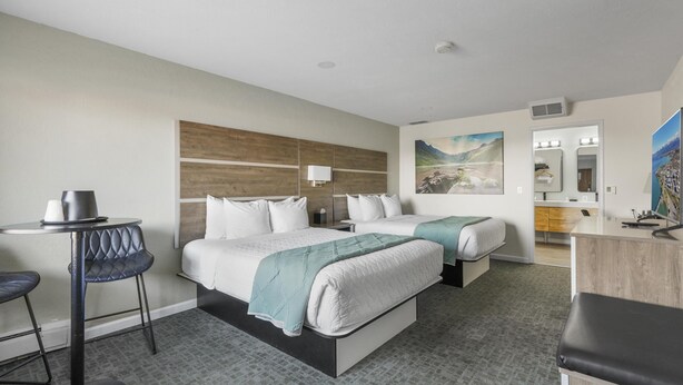 Ein Hotelzimmer mit zwei Betten, einem Schreibtisch, einem Stuhl, einem kleinen Tisch und einem durchgegangenen Tür sichtbaren Badezimmer.