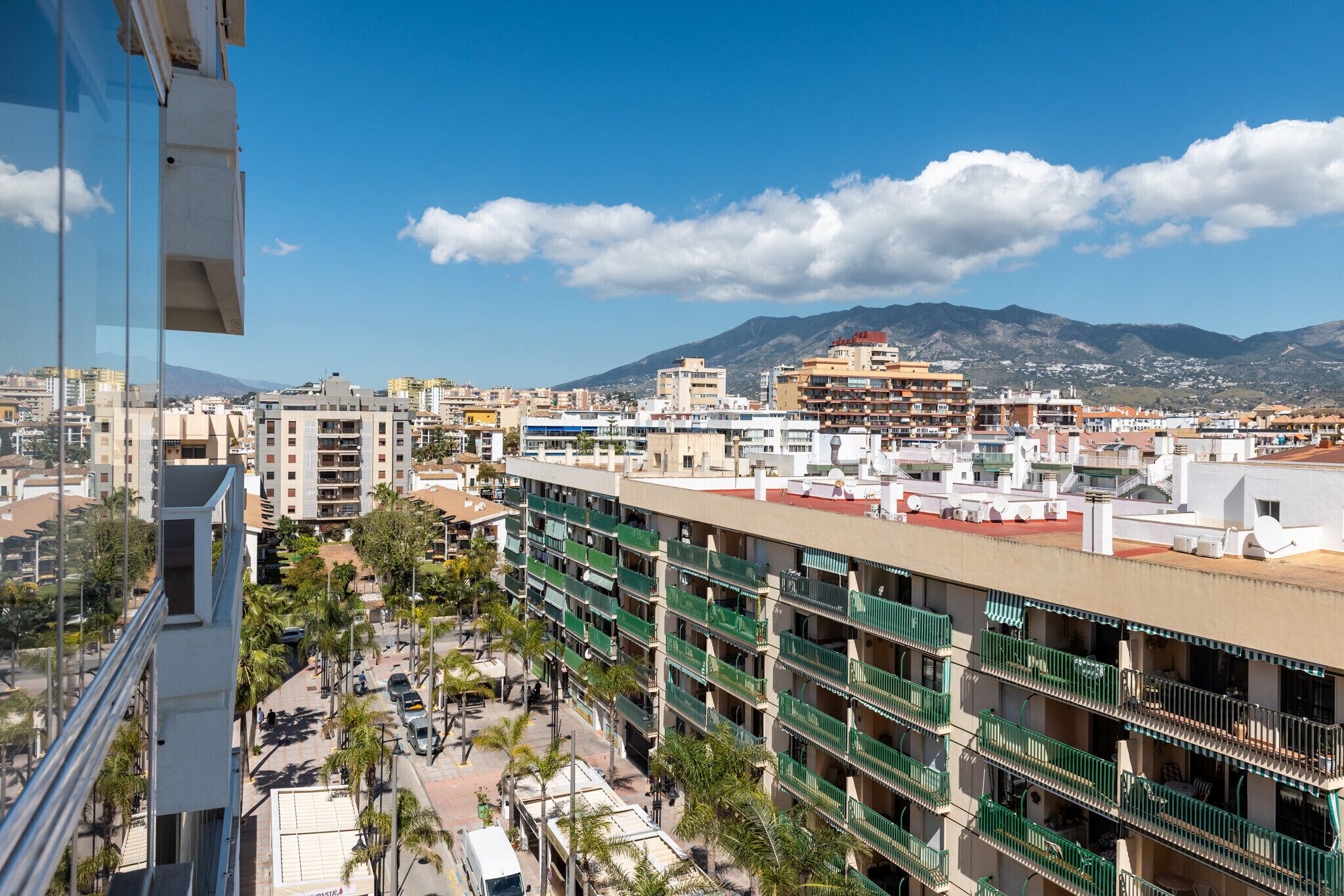 A multi-story building with balconies, a clear sky, and mountains in the background.