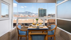 Un balcón con mesa dispuesta para el desayuno, sillas y vistas a edificios y montañas.